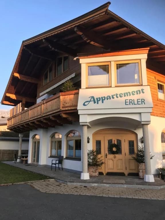 Außenansicht des Appartement Erler in Sankt Johann in Tirol mit Holzbalkonen, Blumenschmuck und Eingangsschild.
