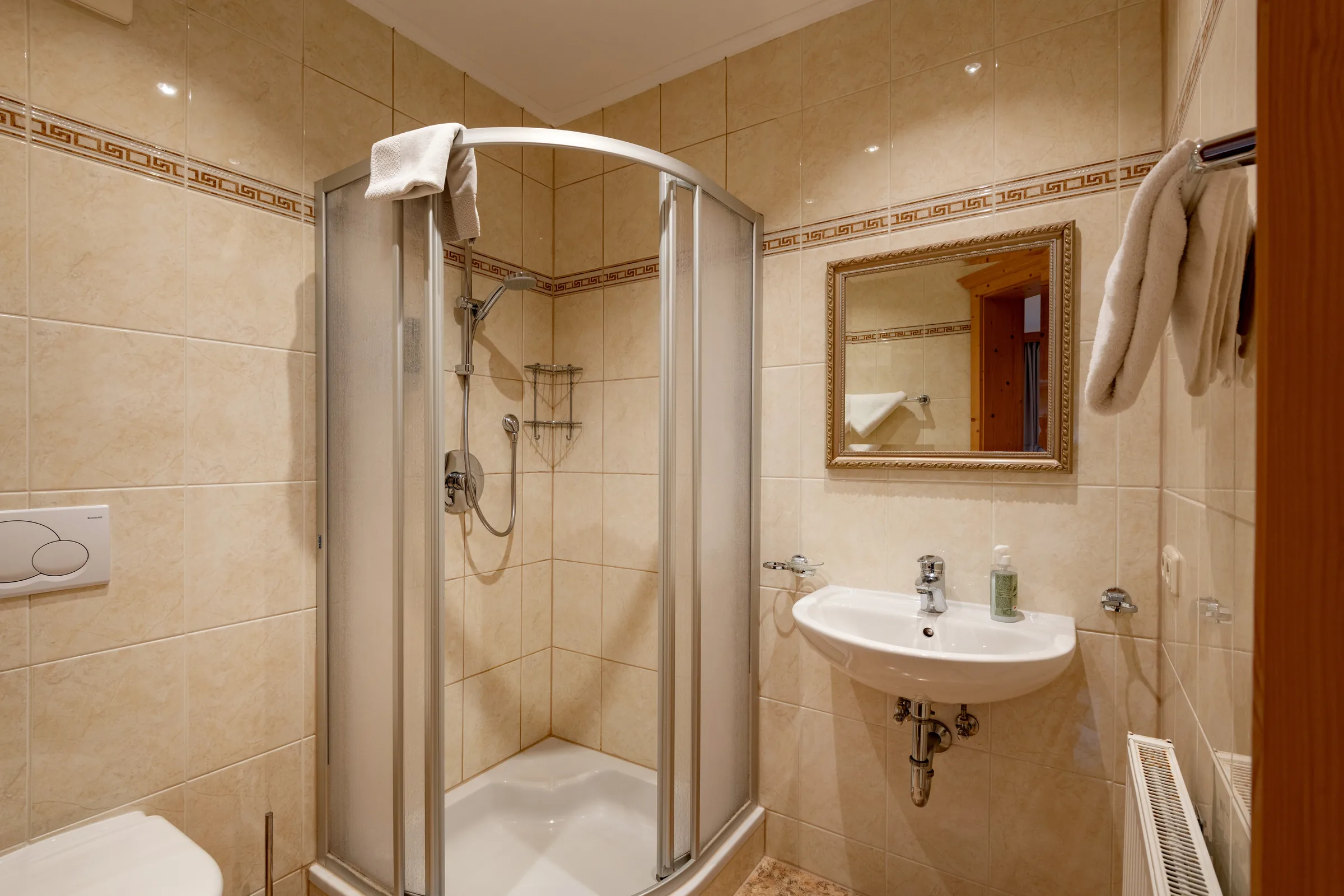 Badezimmer mit bodengleicher Glas-Duschkabine, Holzwaschtisch und dekorativer Fliesen-Bordüre, Appartement mit Terrasse des Appartement Erler.