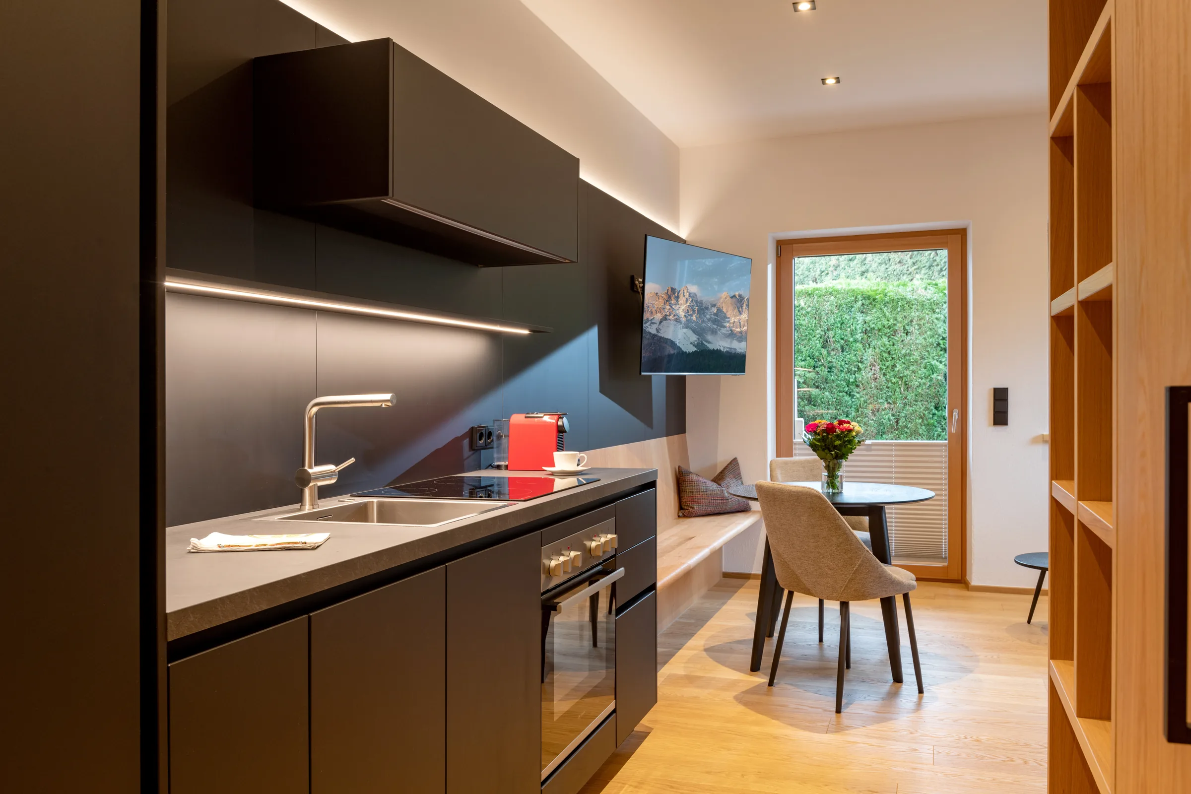 Detailansicht der schwarzen Küche mit LED-Beleuchtung, Backofen und Spüle, Studio mit Garten.