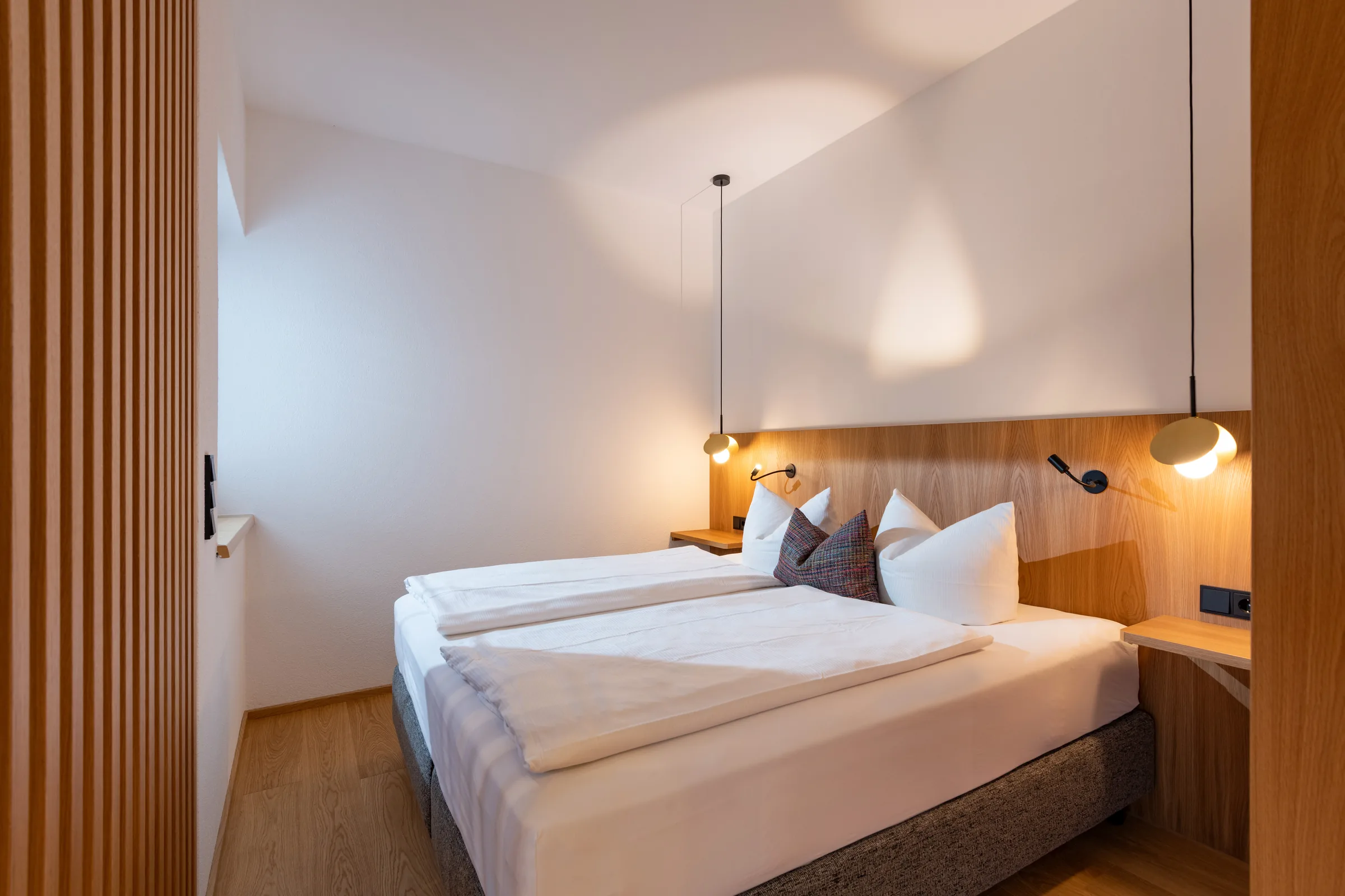 Schlafbereich mit Doppelbett hinter dem Holzlamellen-Raumteiler, Studio mit Garten des Appartement Erler.