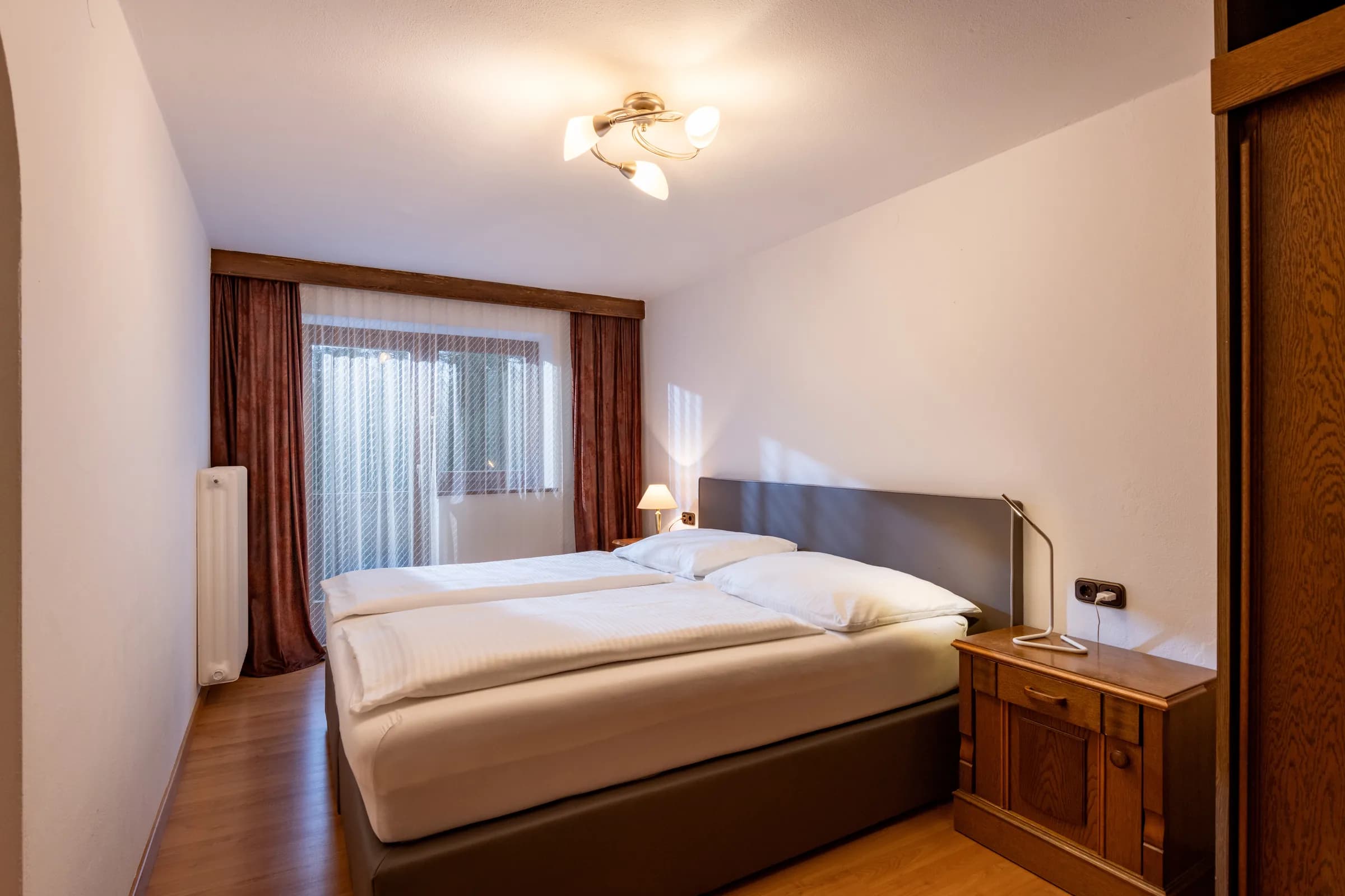 Helles Schlafzimmer mit Doppelbett, weicher Bettwäsche und großem Vorhang-Fenster, Appartement Niederkaiser am Bauernhof Oberlacken.