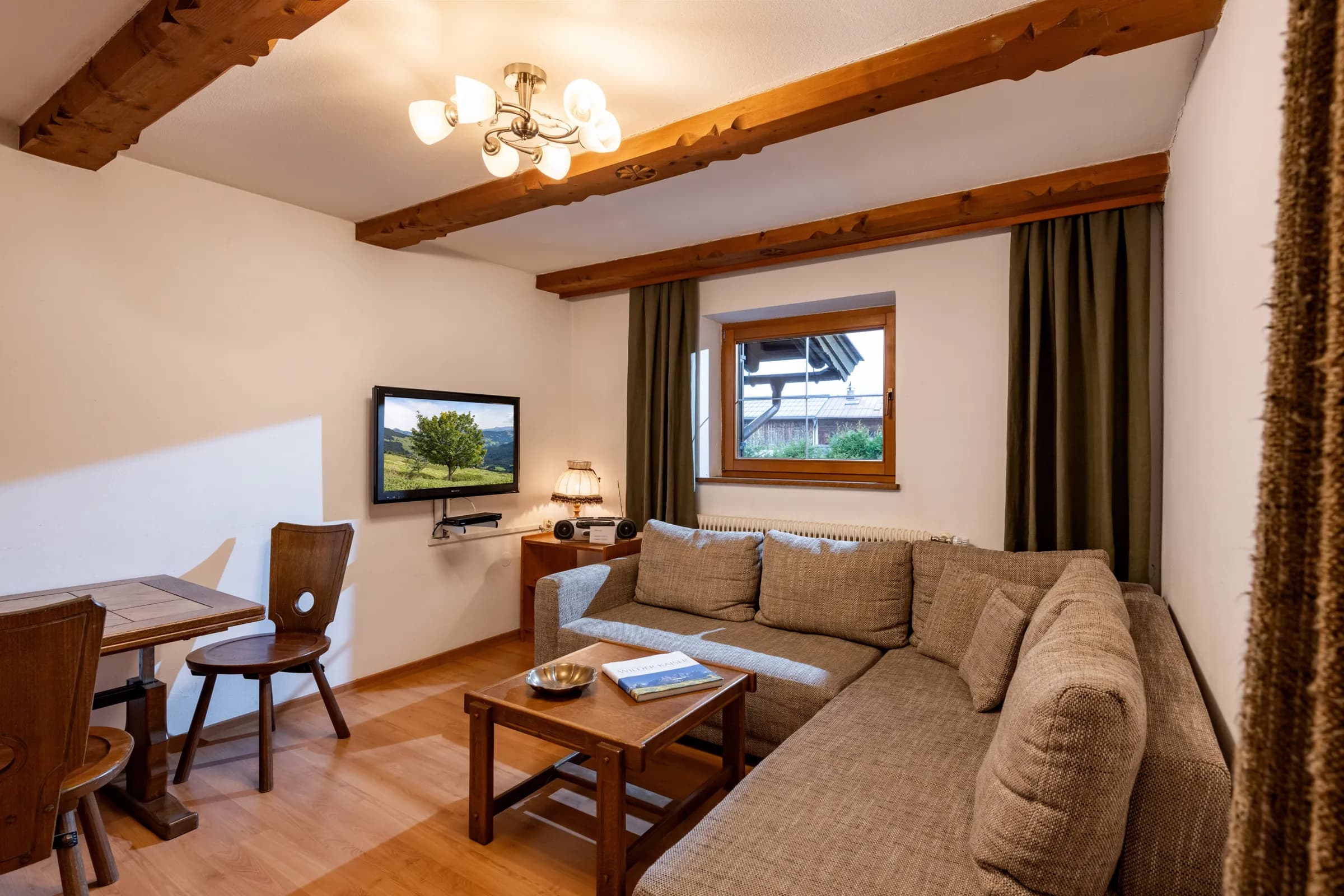 Gemütliches Wohnzimmer mit beiger Eck-Couch, Holzbalken-Decke und rustikaler Sitzecke, Appartement Niederkaiser am Bauernhof Oberlacken.