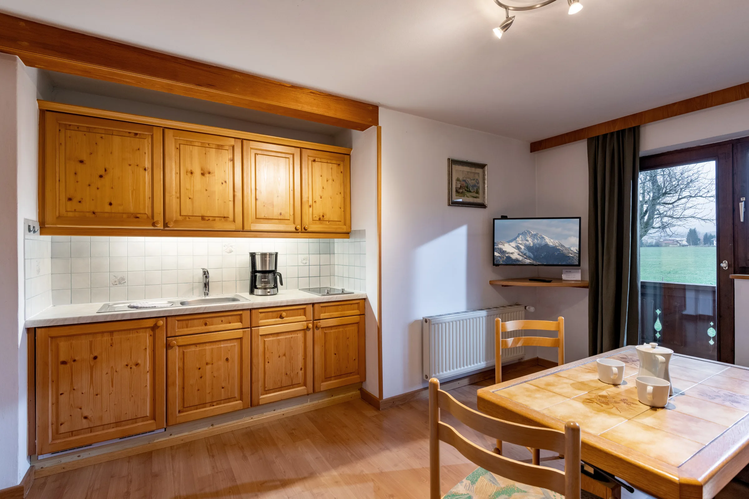 Voll ausgestattete Pinienholz-Küche mit Essplatz, Flachbildfernseher und Zugang zum Balkon mit Bergblick, Appartement Wilder Kaiser.