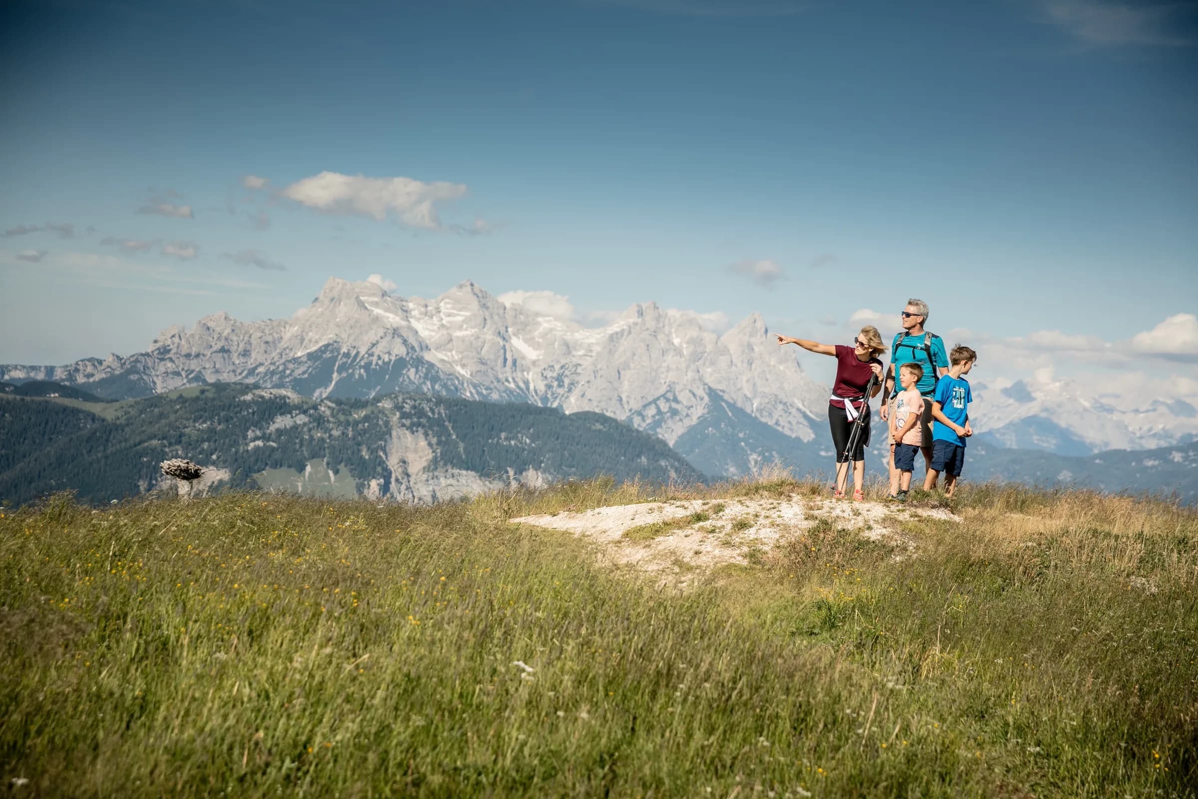 Familie auf einem Bergrücken über dem Tal, vor ihnen die schneebestreute Felswand des Wilden Kaisers.