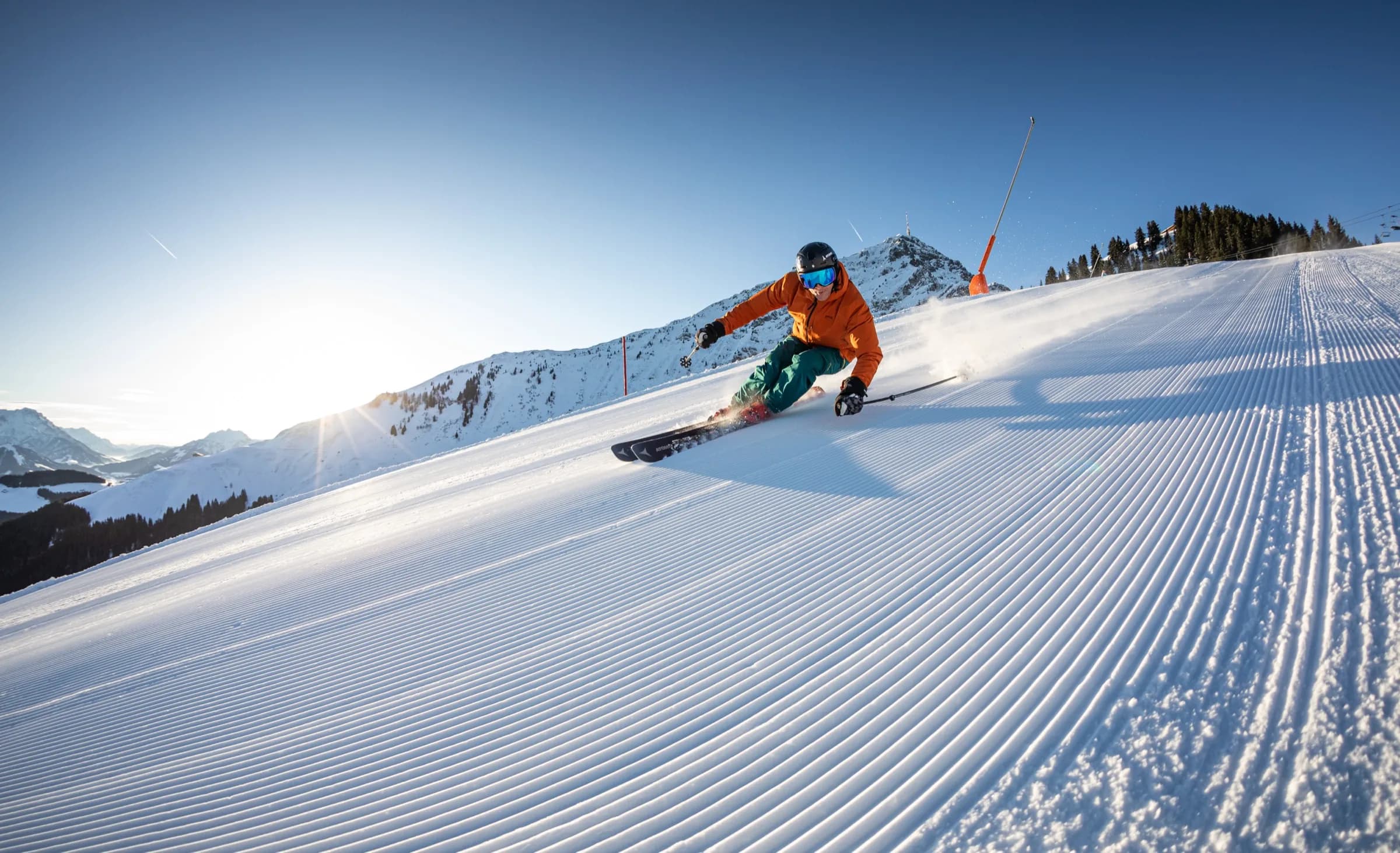 Skifahrer auf einer frisch präparierten Piste im Morgenlicht, die Sonne streift den Schnee.