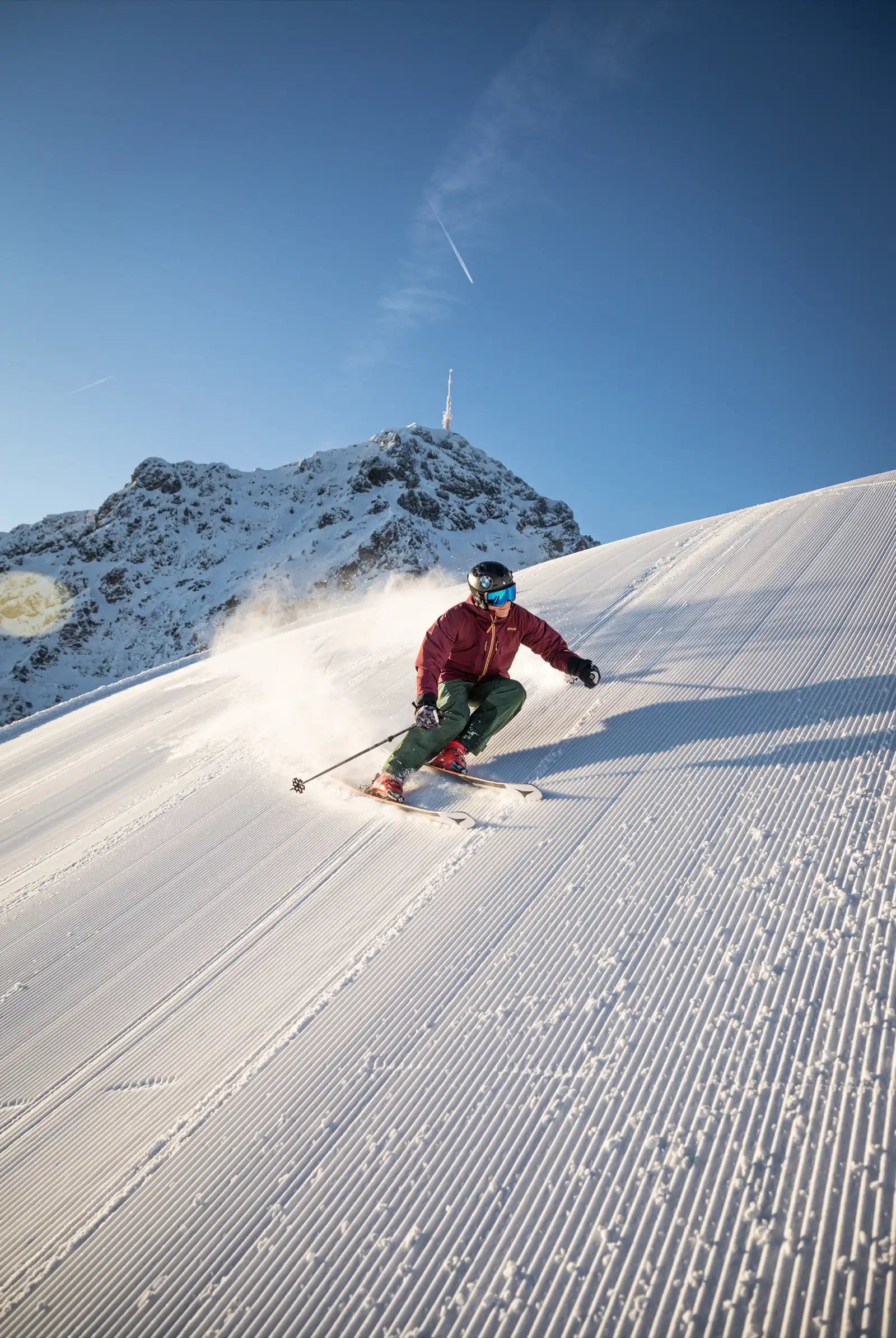 Skifahrer auf einer frisch präparierten Piste im Skigebiet St. Johann, im Hintergrund das Kitzbüheler Horn mit Sendeturm.
