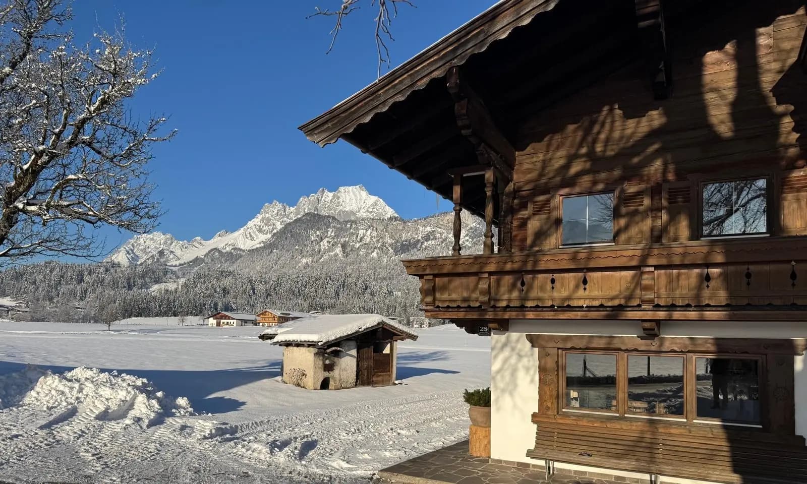 Holzbalkone des Bauernhofs Oberlacken in der Wintersonne, dahinter verschneite Wiesen und der Wilde Kaiser.