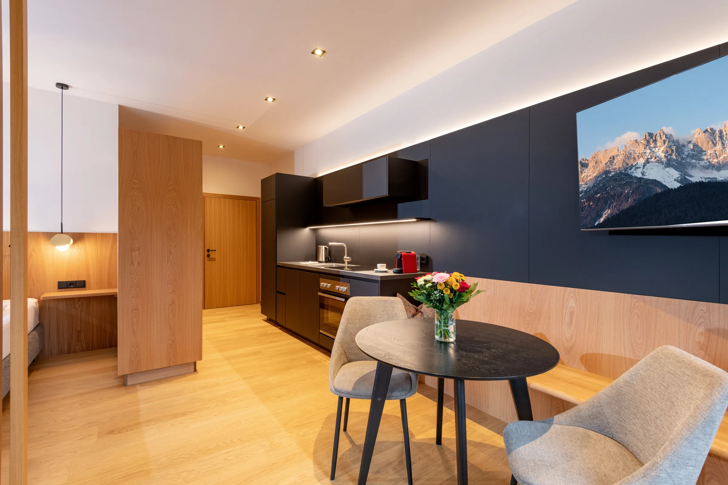 Moderne schwarze Designküche mit Essplatz, Pendelleuchte und Blick auf das Bergpanorama, Studio mit Garten.