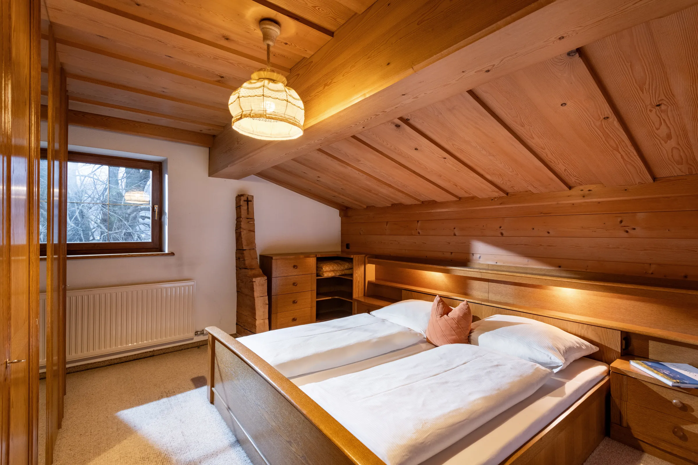 Schlafzimmer mit geschnitztem Pinienholz-Doppelbett und Dachschräge in warmer Pinienholz-Vertäfelung, Appartement Kitzbüheler Horn.