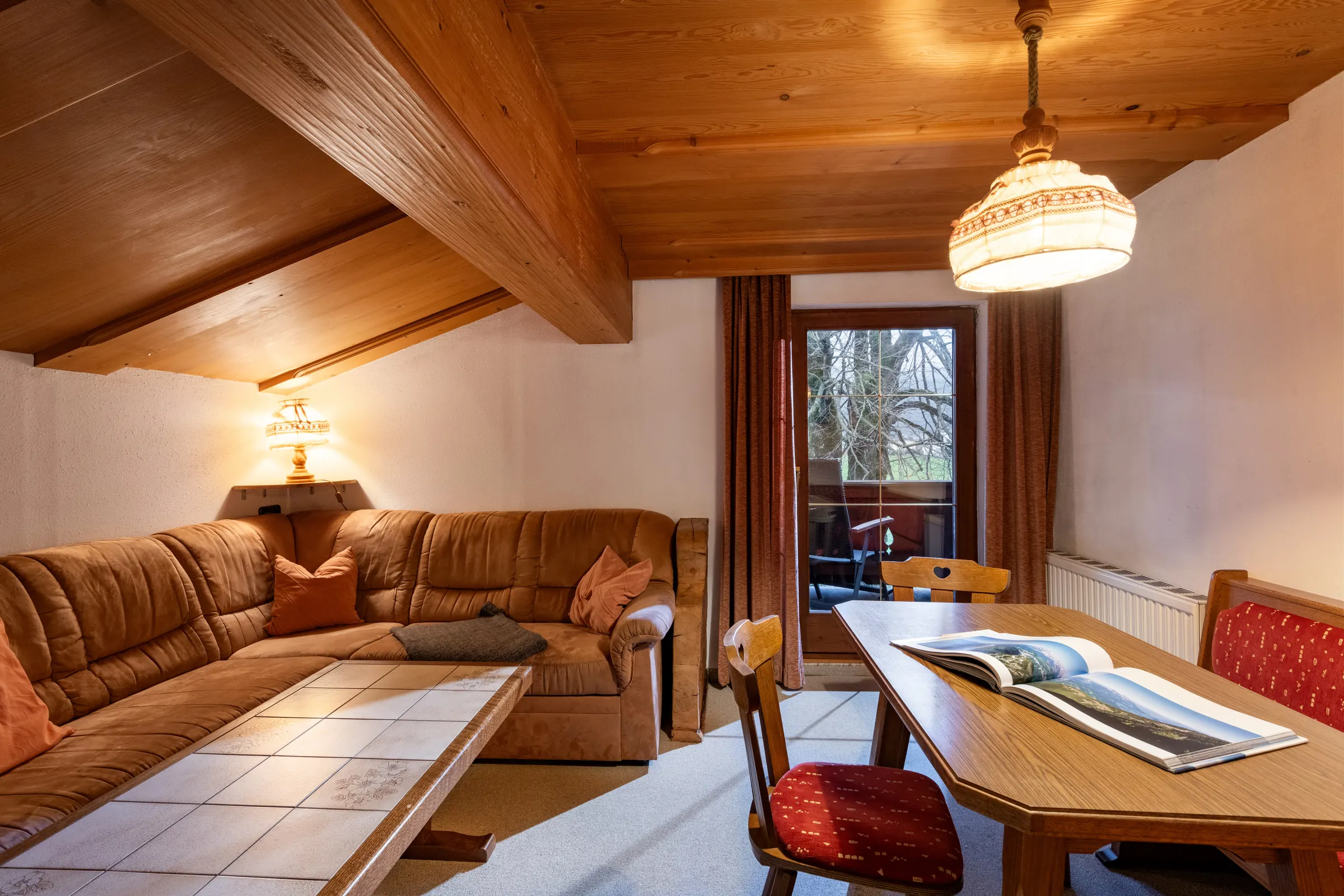 Wohnzimmer mit brauner Ledereck-Couch, gefliestem Couchtisch und Pinienholz-Dachschräge im Appartement Kitzbüheler Horn am Bauernhof Oberlacken.