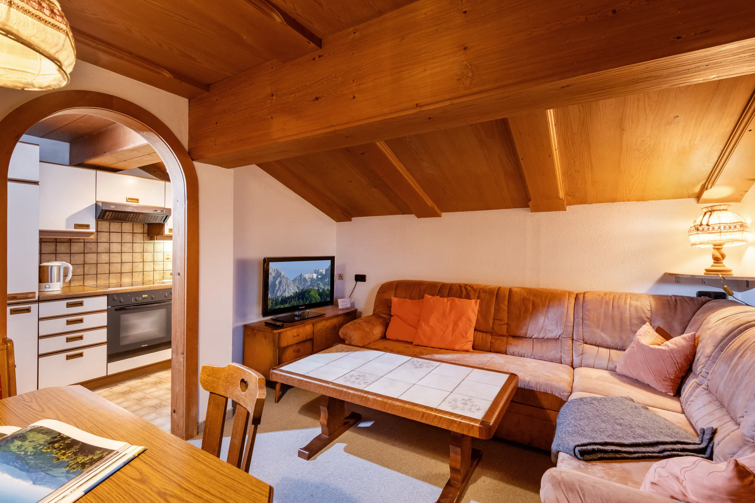 Wohnzimmer mit Ledercouch und Bogendurchgang zur offenen Küche unter Pinienholz-Dachschräge, Appartement Kitzbüheler Horn.