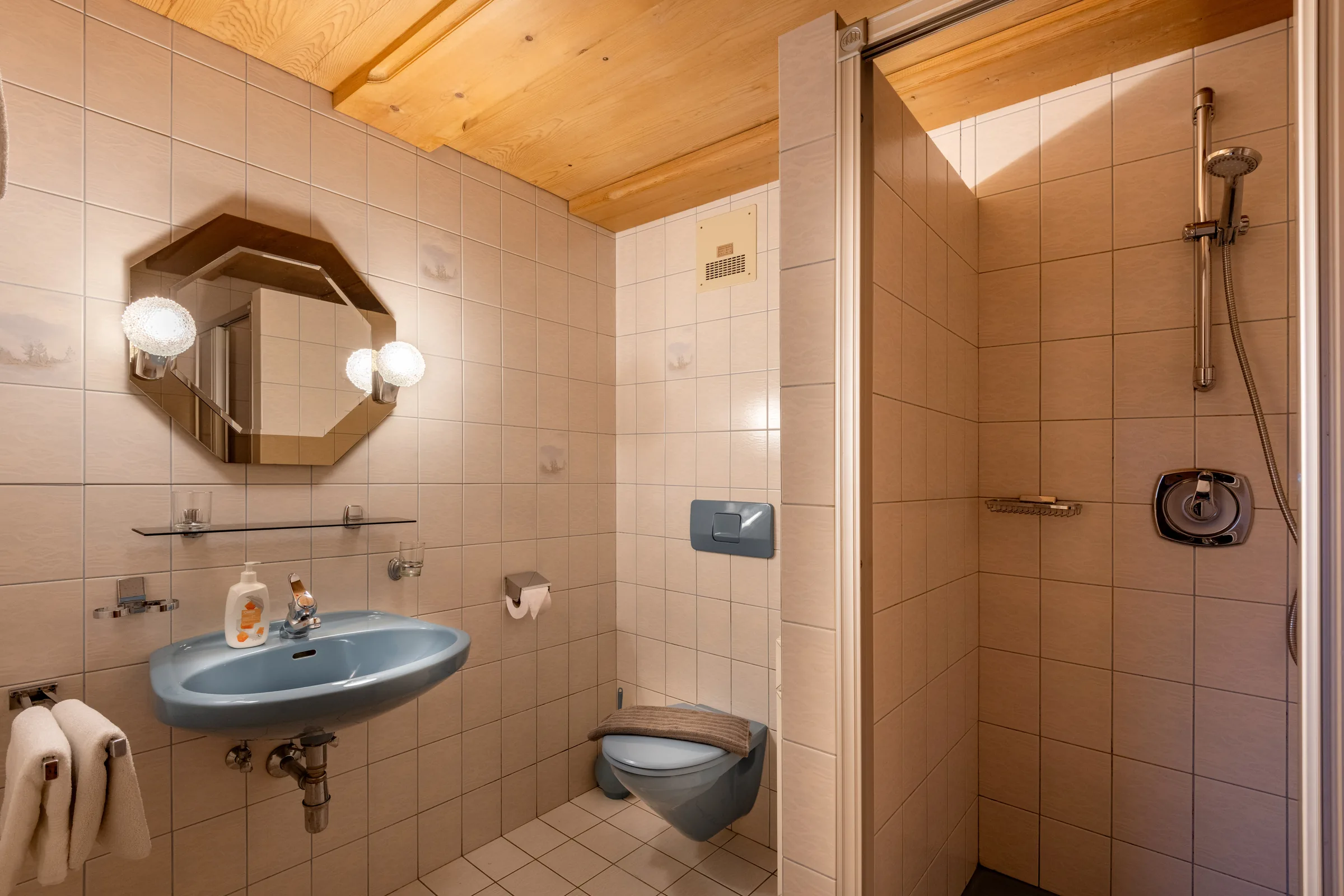 Geräumiges Badezimmer mit bodengleicher Duschkabine und blauem Waschbecken unter Holzdecke, Appartement Wilder Kaiser am Bauernhof Oberlacken.