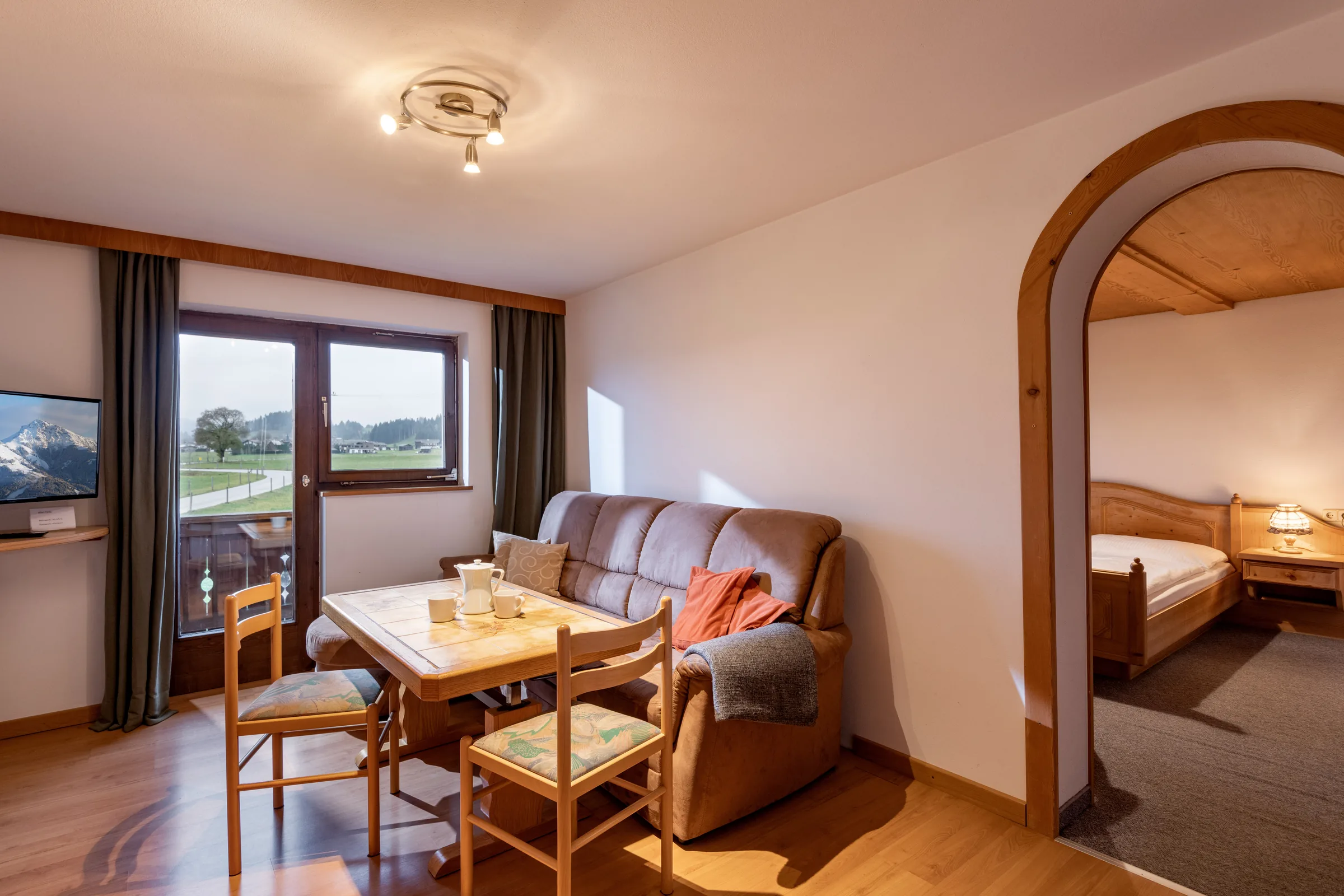 Wohn- und Essbereich mit Couch, Esstisch und Fensterfront mit Blick auf Wiesen und Berge im Appartement Wilder Kaiser am Bauernhof Oberlacken.